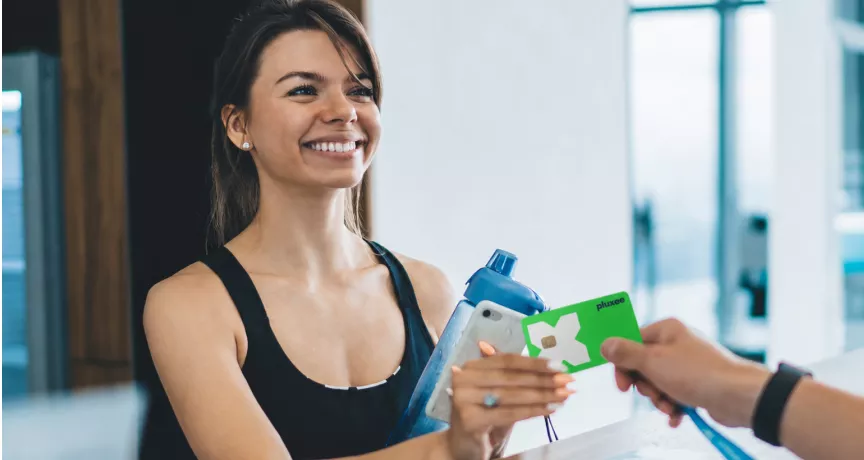 Žena drží Pluxee kartu u recepce fitness centra 