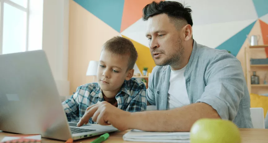 Otec pomáhá synovi s přípravou do školy u notebooku 