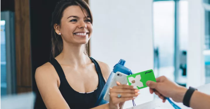Žena drží Pluxee kartu u recepce fitness centra