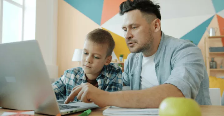 Otec pomáhá synovi s přípravou do školy u notebooku