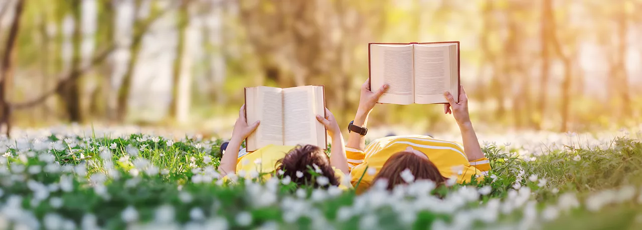 dva lidé s knihou v ruce na louce