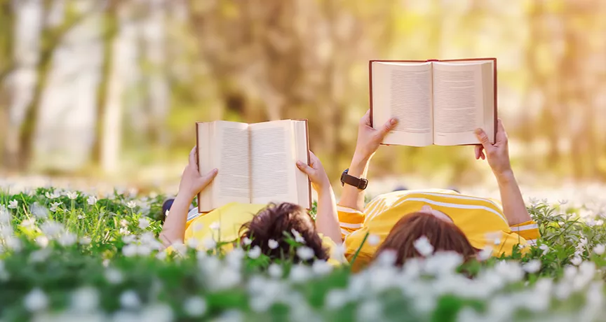 dva lidé s knihou v ruce na louce