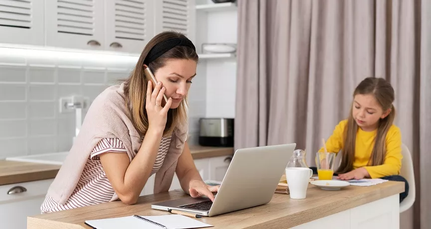 Matka telefonuje a pracuje na notebooku v kuchyni, vedle ní sedí dcera