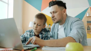 Otec pomáhá synovi s přípravou do školy u notebooku